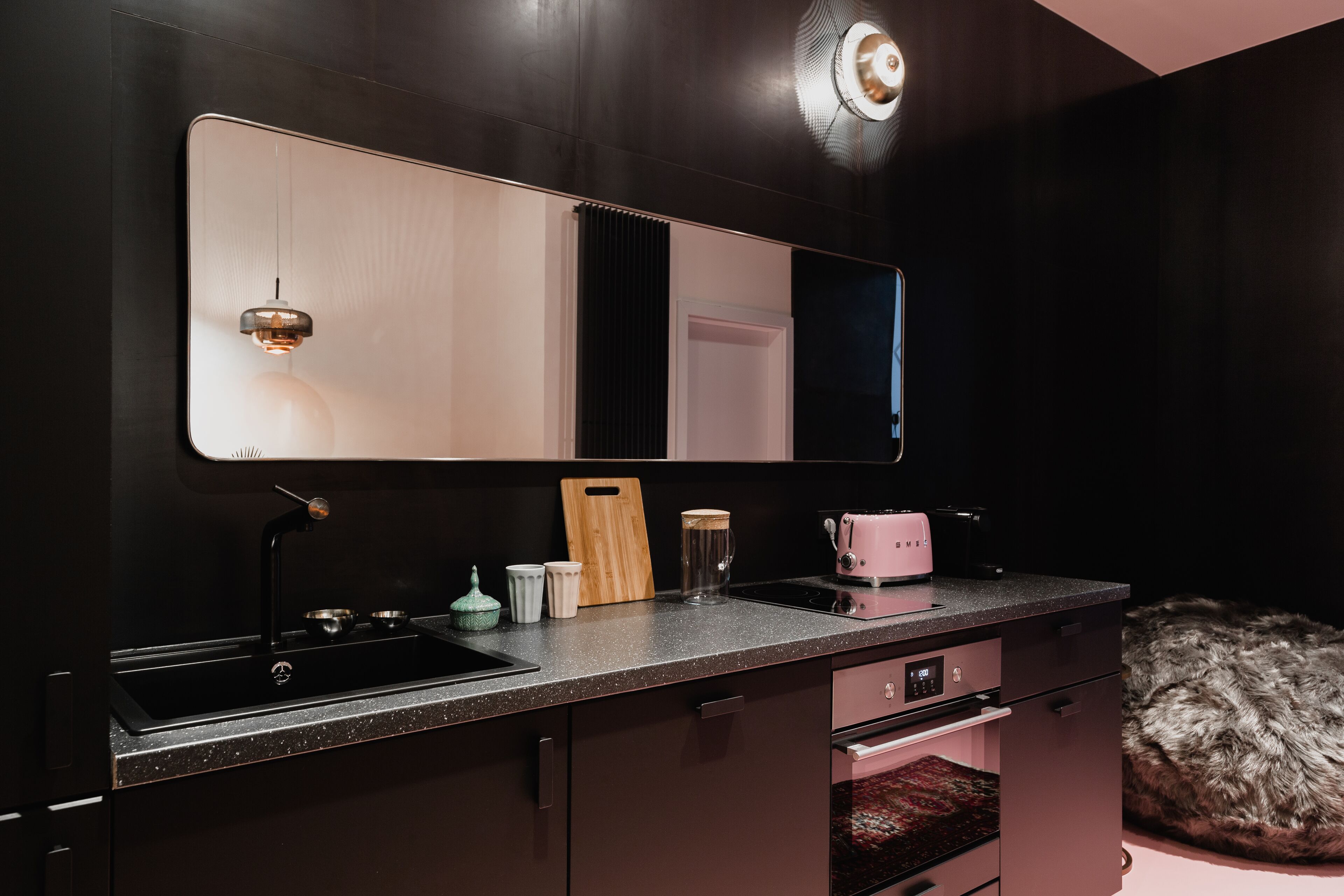 Een moderne keuken met een grote spiegel, een gootsteen, een aanrecht met een broodrooster en een pluizige vloerkleden.