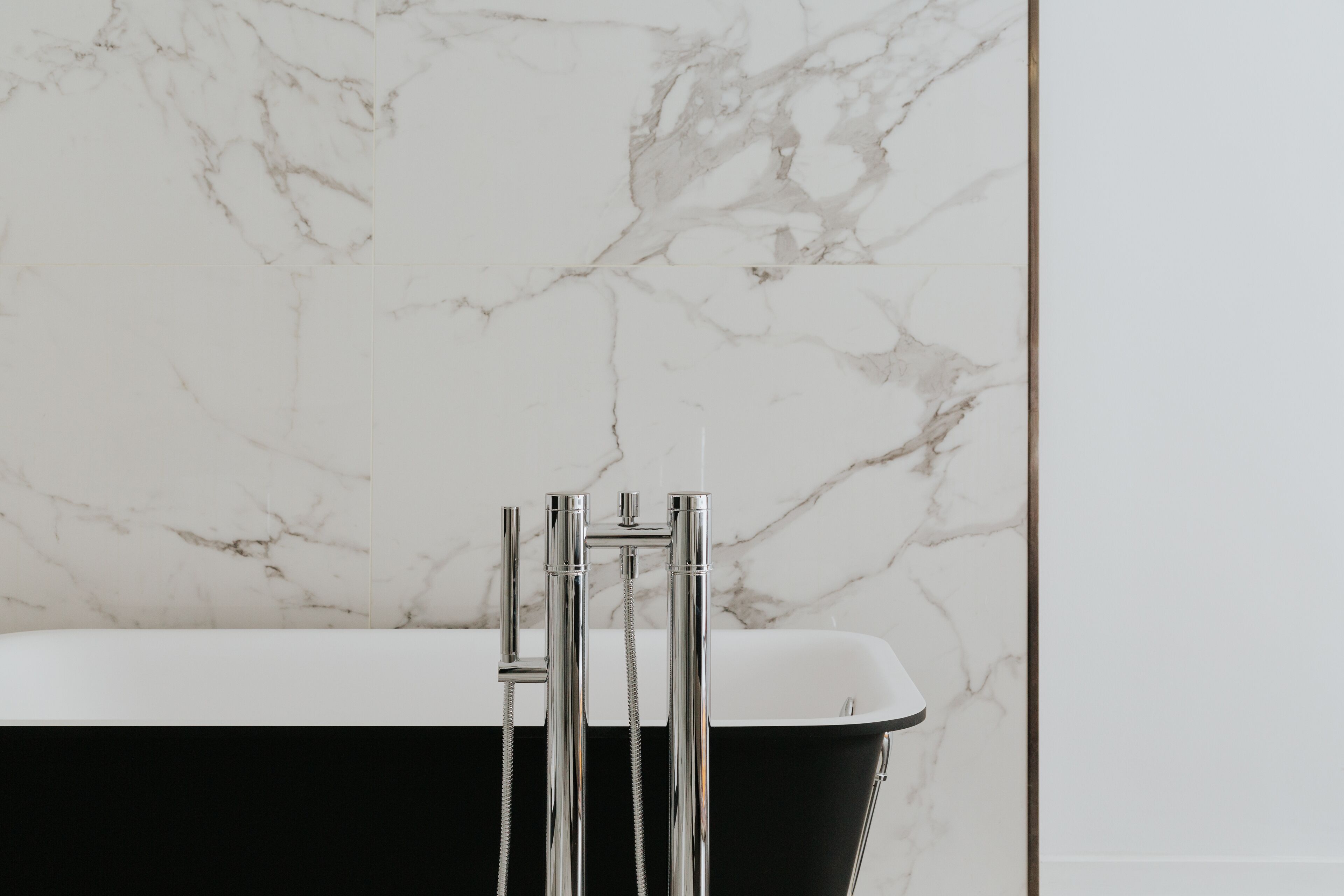 A bathroom with a black bathtub and a white marble wall.