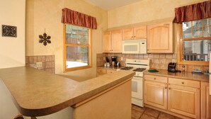 A kitchen with wooden cabinets, a microwave, stove, and a window with curtains. - Comfortable and Cozy 3 Bedroom Townhome (Keystone)