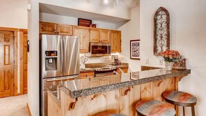A kitchen with wooden cabinets, stainless steel appliances, a granite countertop, and a decorative mirror. - Spacious Private Condo for 6 (Keystone)