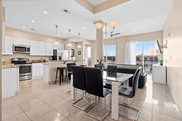 A modern kitchen with white cabinets, stainless steel appliances, and a dining area with a glass table and black chairs.
