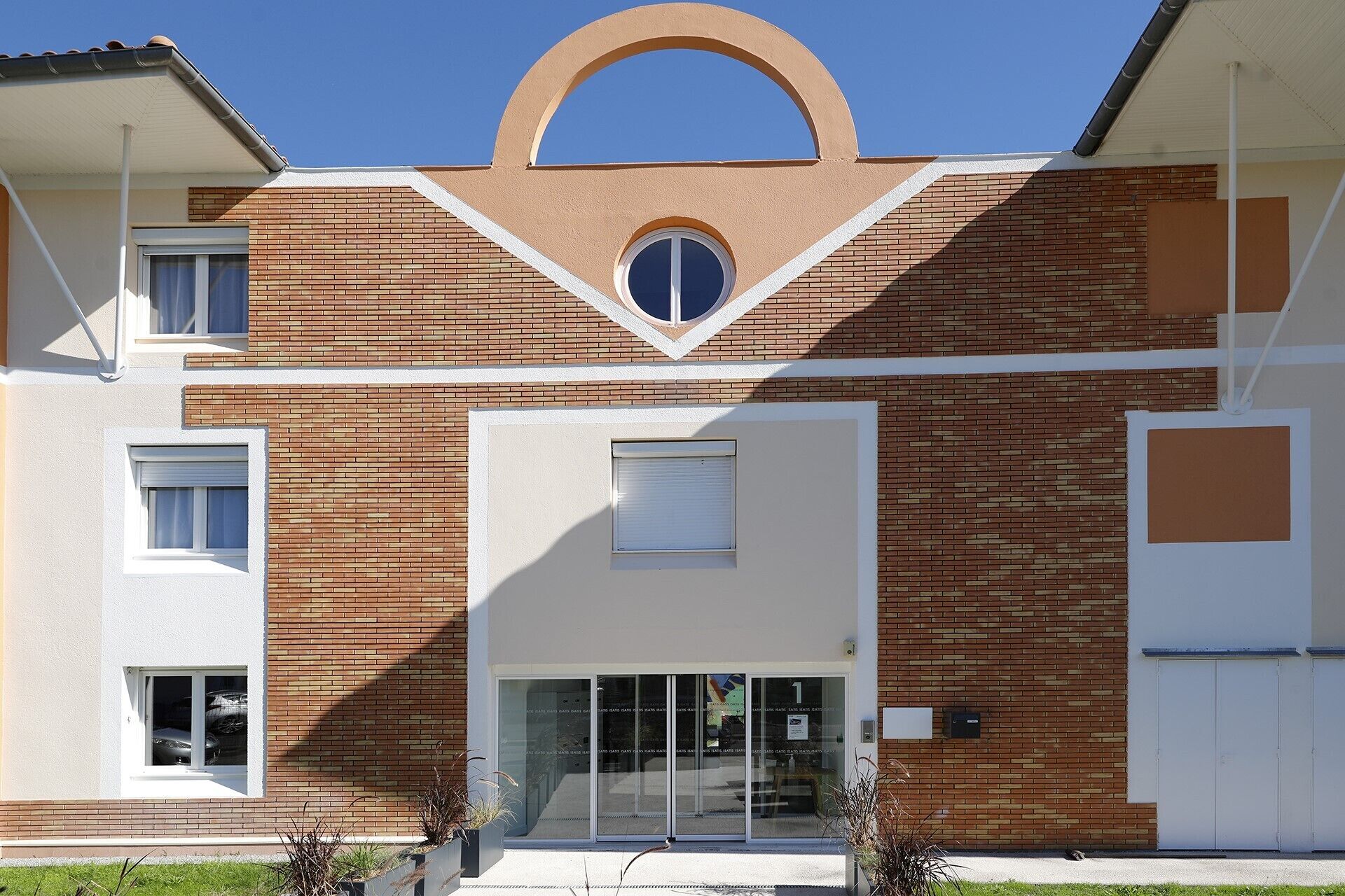 A modern building with a brick facade, a central entrance with glass doors, and a distinctive archway above the entrance.