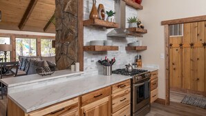 Una cocina con encimera de mármol, armarios de madera, estufa y pared decorativa de piedra.