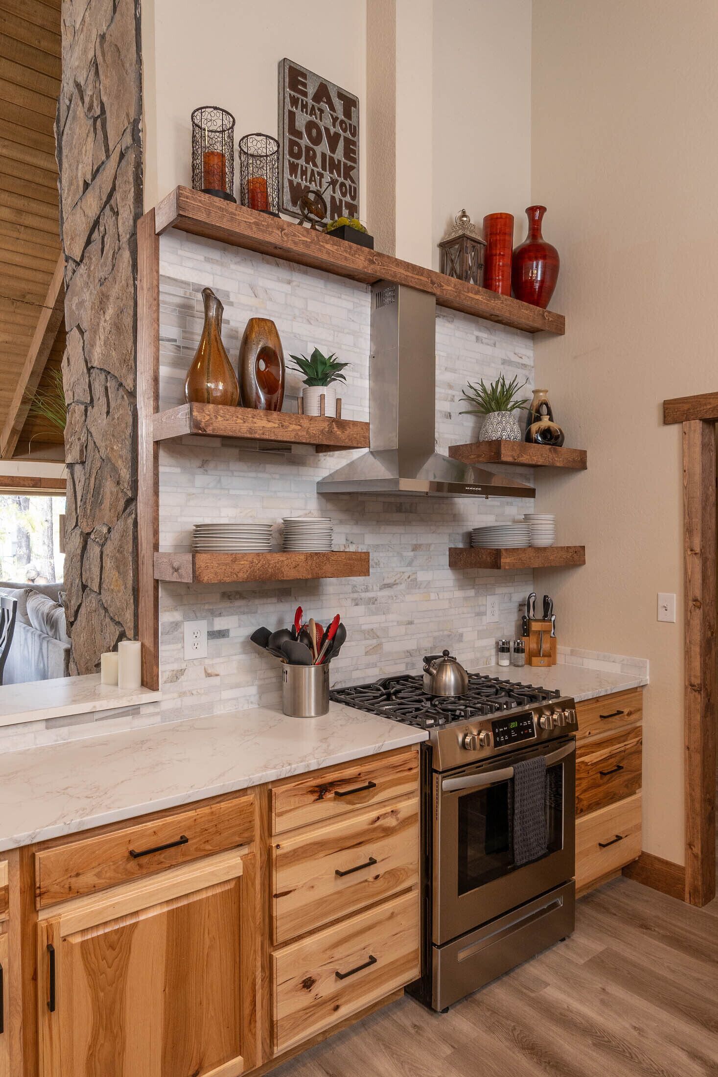 A modern kitchen with wooden cabinets, a stainless steel stove, and decorative shelves.