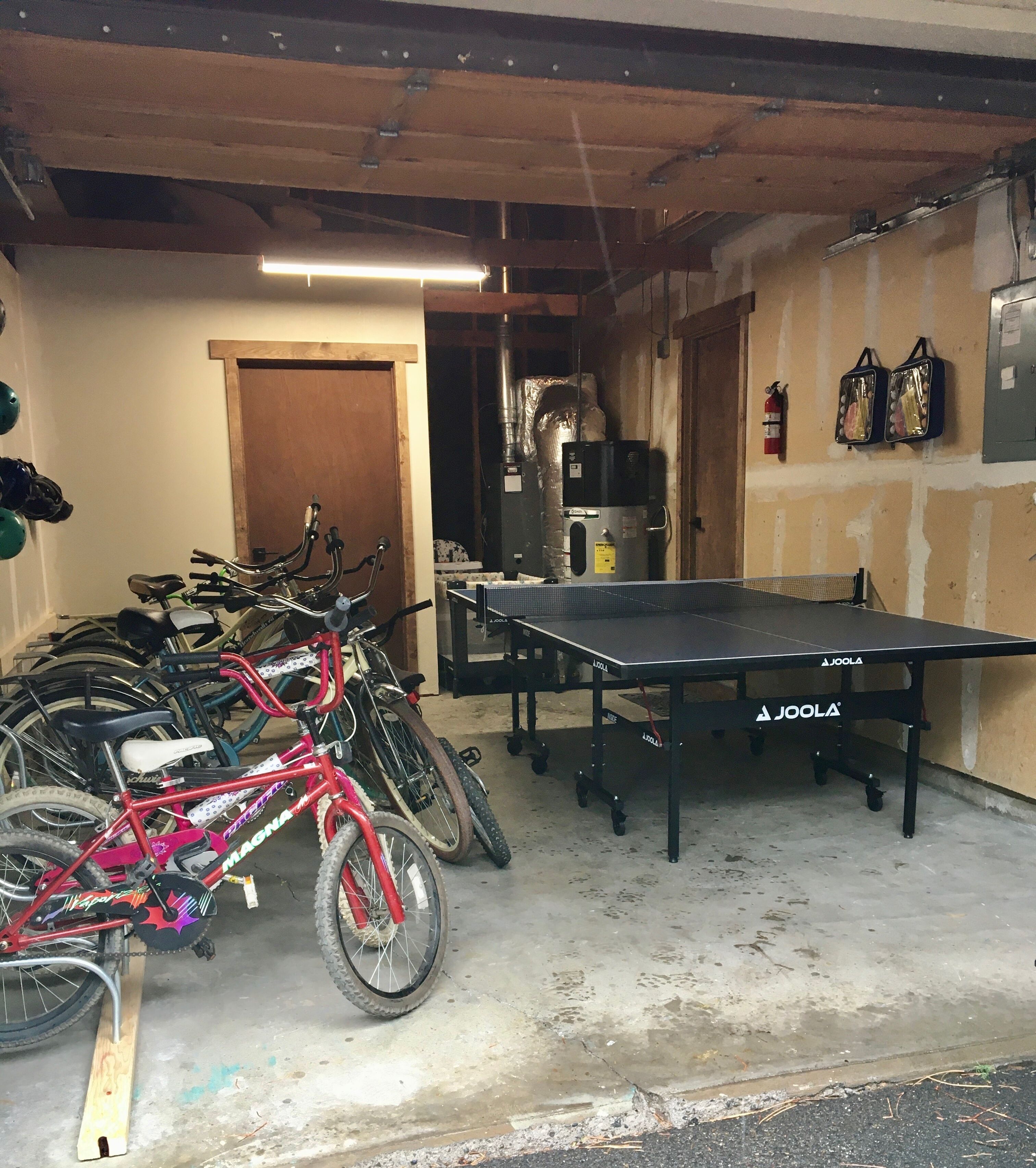 A garage with bicycles, a ping pong table, and a fire extinguisher.
