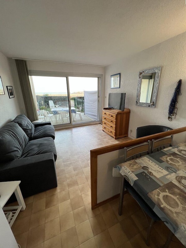 Un espacio habitable compacto con sofá, cómoda de madera pequeña, televisor y balcón con vistas.