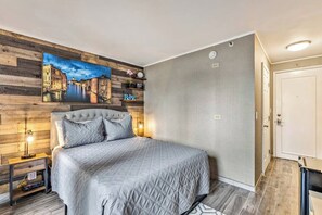 Ein Schlafzimmer mit einem großen Bett, einer Holzwand mit Stadtbildgemälde, einem Nachttisch mit Lampe und einer Tür rechts.