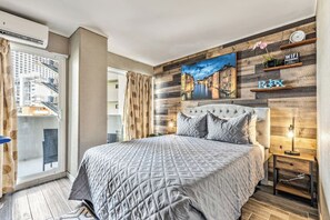 Un dormitorio con una cama grande, un cuadro de la ciudad en la pared, un balcón con vistas a edificios y una estantería de madera con un letrero que dice 'Relax'.