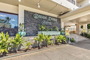 Exterior del Waikiki Grand Hotel con fachada de piedra, una zona de recepción y una escalera que lleva a la entrada.