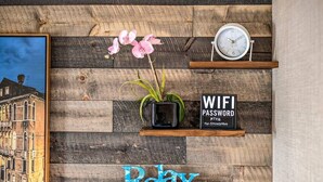 Un mur en bois orné d’un tableau encadré, d’une plante en pot, d’une horloge, d’une pancarte indiquant le mot de passe du réseau Wi-Fi et d’une autre pancarte avec l’inscription « Détendez-vous ».