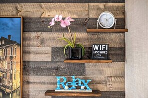 Eine Holzwand mit einem gerahmten Bild, einem Blumentopf, einer Uhr, einem Schild mit einem WLAN-Passwort und einem Schild mit der Aufschrift 'Relax'.