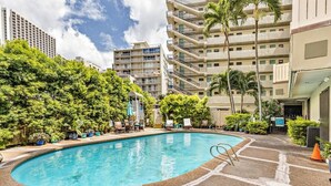 Une piscine entourée d’une végétation luxuriante et un immeuble à plusieurs étages doté de balcons.
