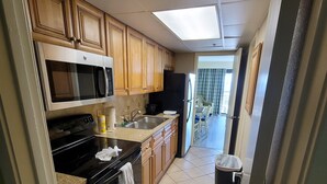 A kitchen with wooden cabinets, a black stove, a microwave, a sink, and a trash can. - Oceanfront Suite, Myrtle Beach SC (Myrtle Beach)