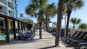 A wooden boardwalk with sun loungers and palm trees, leading to a pool area. - Oceanfront Suite, Myrtle Beach SC (Myrtle Beach)