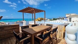 A wooden deck with a table and chairs, a pergola, and a view of the ocean. - Casa Reyes at La Diosa - Stunning Roof Top Ocean view (Isla Mujeres)