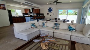 A modern living room with a sectional sofa, a glass coffee table, and a kitchen in the background. - Casa Reyes at La Diosa - Stunning Roof Top Ocean view (Isla Mujeres)