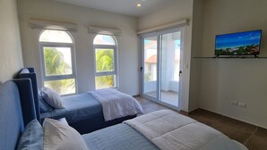 A bedroom with two beds, large windows, a sliding glass door, and a TV on the wall. - Casa Reyes at La Diosa - Stunning Roof Top Ocean view (Isla Mujeres)