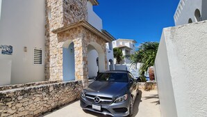 A narrow street with a stone wall and a parked Mercedes-Benz. - Casa Reyes at La Diosa - Stunning Roof Top Ocean view (Isla Mujeres)