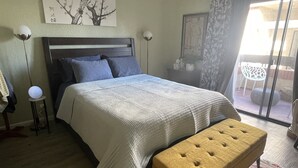 Et soveværelse med seng, bænk, natbord og en lampe på væggen.