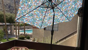 En balkon med fletstole, et lille bord og en farverig parasol.