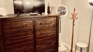 Et træskab med skuffer, et fladskærms-tv, en ventilator og et knagered i et rum med strukturerede vægge.