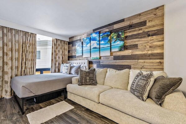 A bedroom with a bed, a sofa, a wooden wall panel, and a window with curtains.