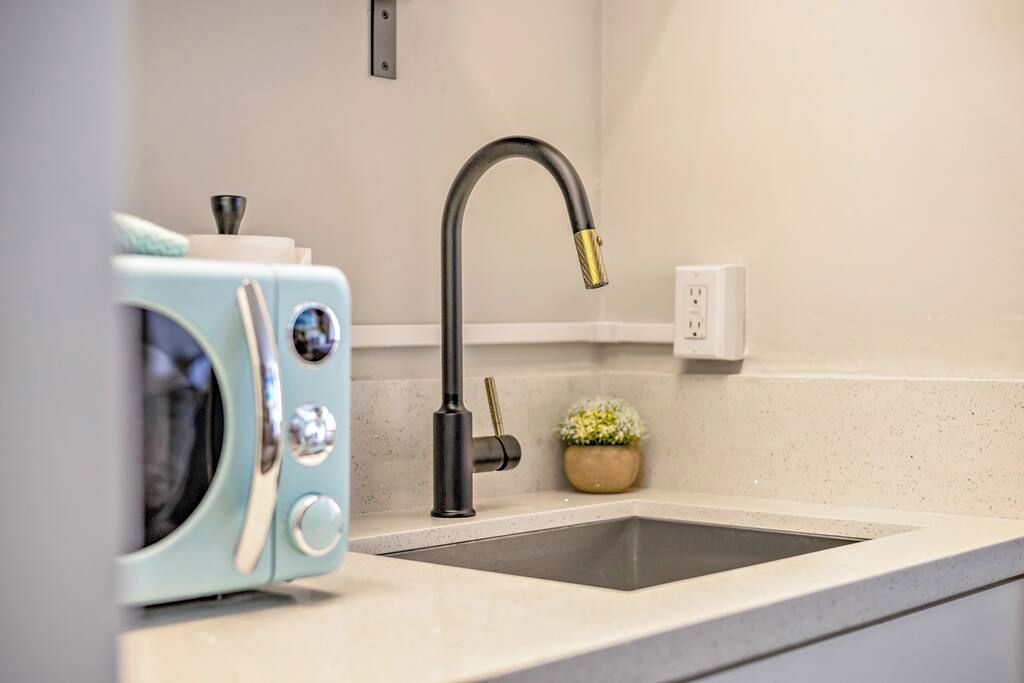 Een keuken met een moderne kraan, een magnetron en een kleine plant in een pot op het aanrecht.