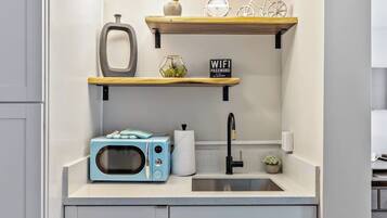 Een keuken met een magnetron, spoelbak en houten planken met diverse spullen.
