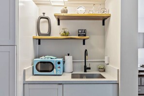 A kitchen with a microwave, sink, and wooden shelves with various items.