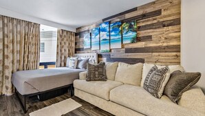A bedroom with a bed, a sofa, a wooden wall panel, and a window with curtains.