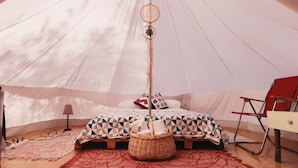 Una carpa con una cama, un tapete rojo estampado, una cesta de mimbre, una lámpara y una silla roja.