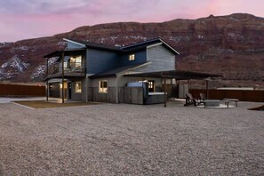 A modern two-story house with a large patio area, a hot tub, and a view of a mountain range. - Slick Rock Retreat House (Moab)