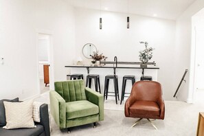 A modern living room with a green armchair, a brown leather chair, and a dining area with stools and a bar. - Slick Rock Retreat House (Moab)