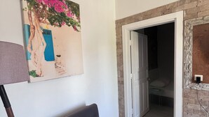 Una habitación con un sofá gris, un cuadro de un árbol y una puerta azul, además de una pared de ladrillo.