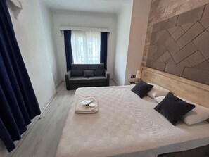 A hotel room with a bed, a sofa, a window with curtains, and a stone-patterned wall. - HANBABA HOTEL (Bodrum)