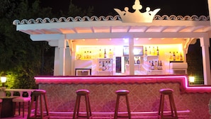 Un bar al aire libre con un toldo blanco, una decoración con forma de corona y tres taburetes.