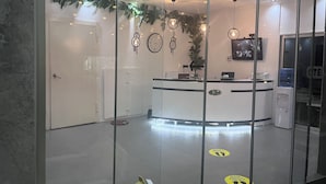 Un área de recepción con un separador de vidrio, mostrador de recepción, un reloj y dispensador de agua.