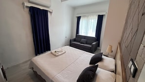 Habitación de hotel con cama, sofá, aire acondicionado, ventana con cortinas y lámpara.