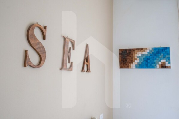 Wooden letters spelling "SEA" on a wall, with a pixelated artwork to the right.