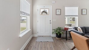 A living room with a door, a window, a plant, a couch, and a small table.