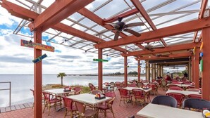 An outdoor restaurant with tables and chairs, a glass ceiling, and a view of the water.