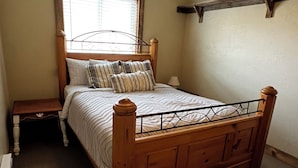 A bedroom with a wooden bed, a nightstand, a ceiling fan, and a window with blinds. - Hilltop riverview bunkhouse (Riggins)