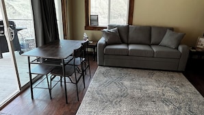 A living room with a sofa, a dining table with chairs, a rug, and a window with a view of mountains. - Hilltop riverview bunkhouse (Riggins)