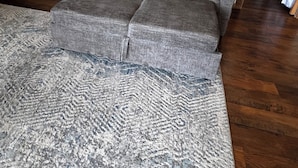 A living room with a grey sectional sofa, a patterned rug, a flat-screen TV, and a wooden shelf with various items. - Hilltop riverview bunkhouse (Riggins)