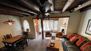 A spacious living area with a wooden dining table, two armchairs, a sofa, and a ceiling fan.