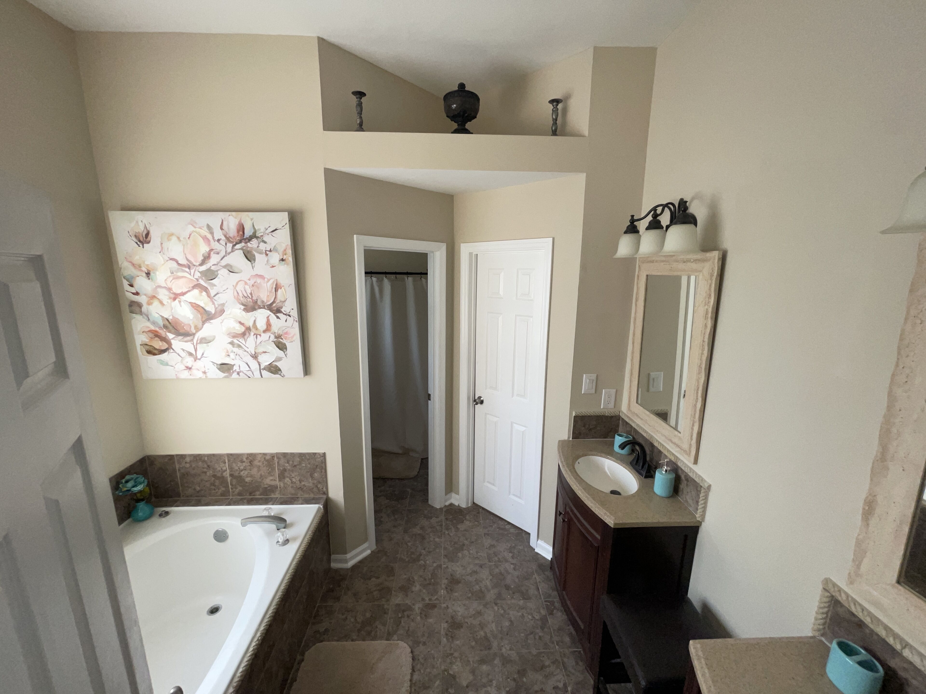 A bathroom with a bathtub, a sink, a mirror, and a door leading to another room.