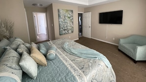 Une chambre à coucher comprenant un lit, un ventilateur de plafond, un téléviseur et une porte donnant sur une autre pièce.