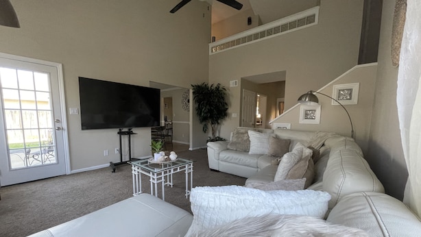 Un salon avec un canapé blanc, une table basse en verre, un téléviseur et un ventilateur de plafond.