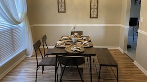 Une salle à manger avec une table en bois dressée pour quatre personnes, flanquée de deux appliques murales décoratives et d’un lustre.