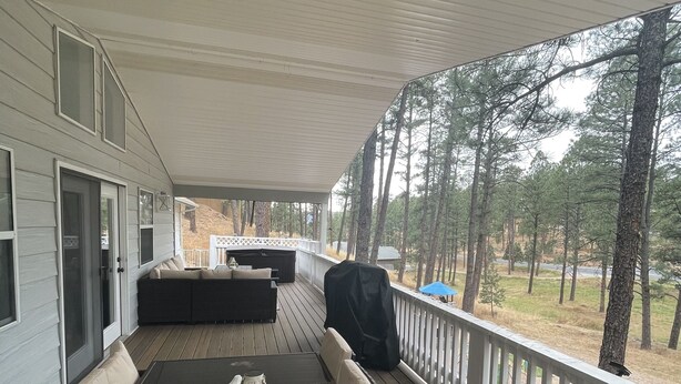 A covered outdoor deck with a dining table and seating, overlooking a wooded area.